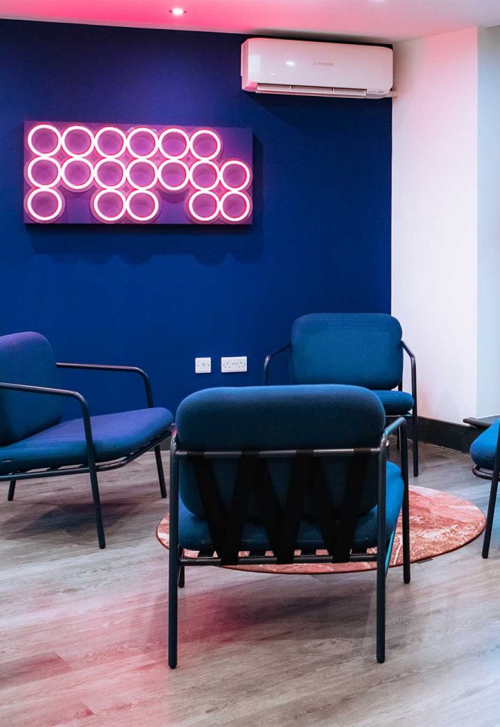 Pink neon sign hanging on the wall, with royal blue chairs and wall